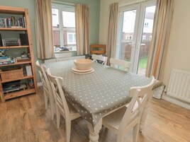 Un comedor con mantel de lunares, sillas blancas, una estantería de madera y una ventana con cortinas.