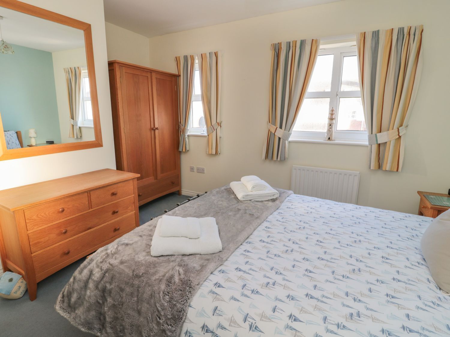 A bedroom with a bed, a wooden dresser, a mirror, and curtains.