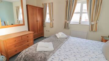 A bedroom with a bed, a wooden dresser, a mirror, and curtains.