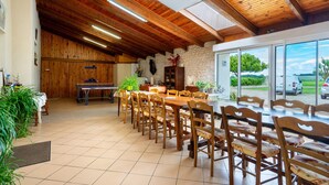 A dining area with wooden tables and chairs, a ping pong table, and potted plants. - Studio at the Farm – Peaceful Retreat for 2 Guests (Semussac)