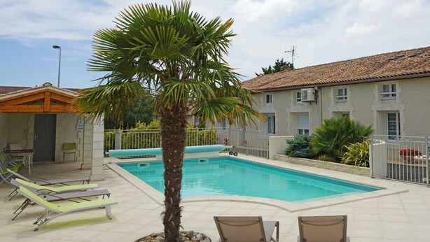 A swimming pool with lounge chairs, a palm tree, and a building with a tiled roof. - Studio at the Farm – Peaceful Retreat for 2 Guests (Semussac)