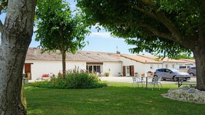 A white building with a tiled roof, a grassy lawn, and a table with chairs. - Studio at the Farm – Peaceful Retreat for 2 Guests (Semussac)