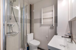 A bathroom with a glass-enclosed shower, a white toilet, a white sink, and a towel rack.