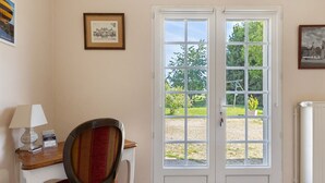 A room with a double door, a chair, a table with a lamp, and framed pictures on the walls. - Bed and Breakfast 'Chambre Lavande' with Shared Pool, Shared Garden and Wi-Fi (Le Controis-en-Sologne)