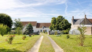 A rural setting with a dirt path leading to a white building with a red-tiled roof, surrounded by greenery and a greenhouse. - Bed and Breakfast 'Chambre Lavande' with Shared Pool, Shared Garden and Wi-Fi (Le Controis-en-Sologne)
