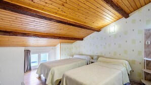 A room with wooden ceiling beams, two beds with matching bedding, a window with curtains, and a wall with notes. - Family Guest Room Anis (Semussac)