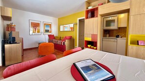 Een kleine hotelkamer met een eettafel, een bank, een kitchenette en een bed.