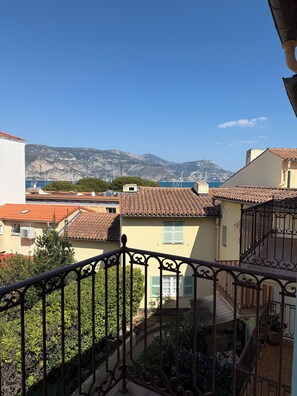 A balcony with a view of a coastal town, buildings with red-tiled roofs, and a mountain in the distance. - Charming apartment with terrace & harbor view - Saint Jean Cap Ferrat (Saint-Jean-Cap-Ferrat)
