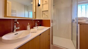 Een moderne badkamer met twee wasbakken, een grote spiegel, een douchecabine en houten kastjes.