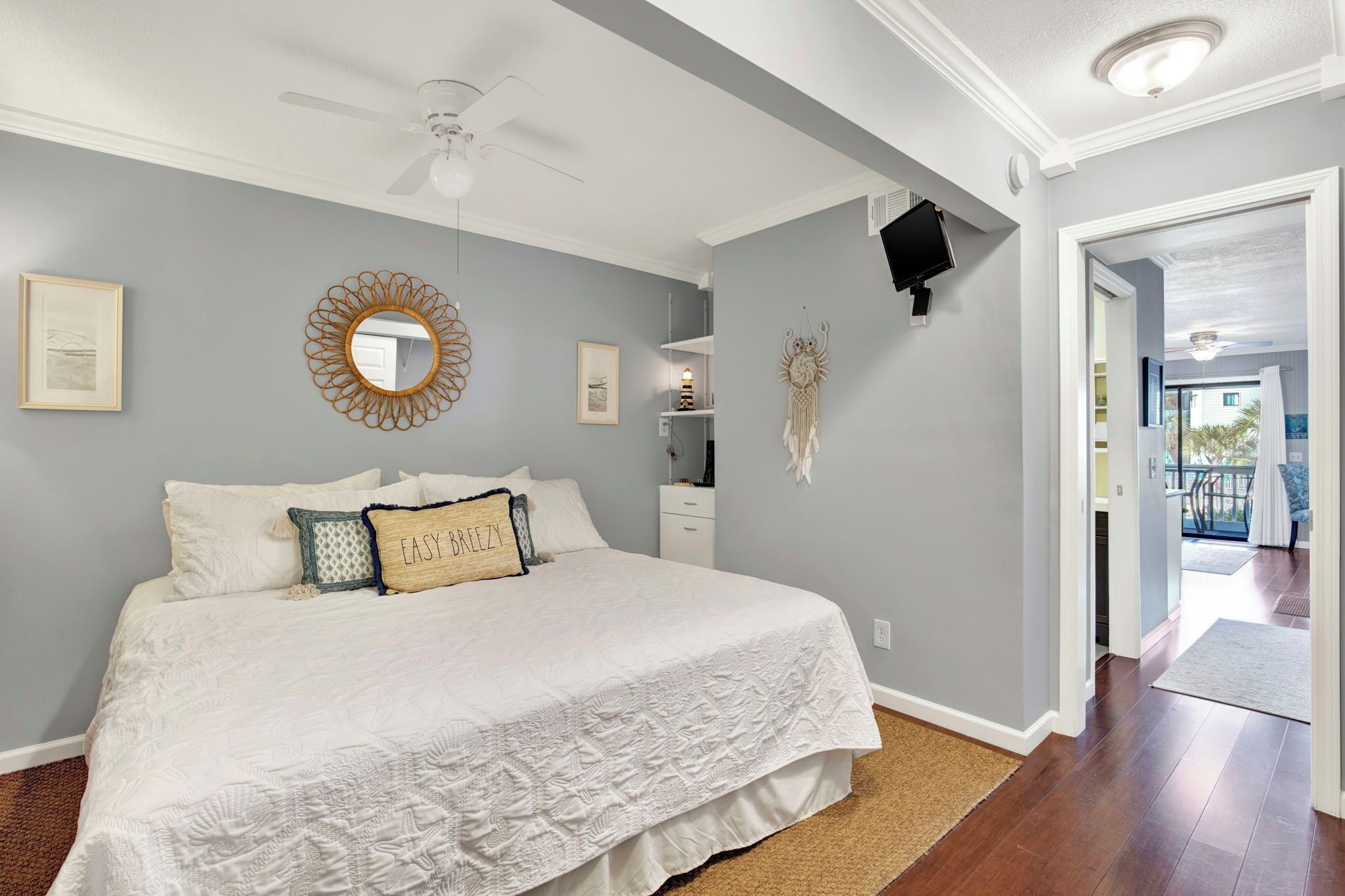 A bedroom with a large bed, a ceiling fan, a wall-mounted TV, and a view to the outside.