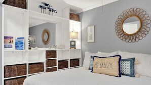 Una camera da letto con un letto grande, biancheria bianca e cuscini decorativi. È presente un armadio a muro con cesti in vimini e uno specchio sulla parete.