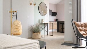Una camera d'albergo moderna con un letto, un angolo salotto con una poltrona, un tavolino, una pianta in vaso e una televisione sullo sfondo.