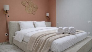 Un letto rifatto con lenzuola bianche e una coperta beige, due lampade a parete e un elemento decorativo a parete.