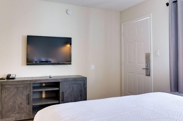 Una habitación de hotel con una cama, un televisor montado en la pared, un armario de madera y una puerta.