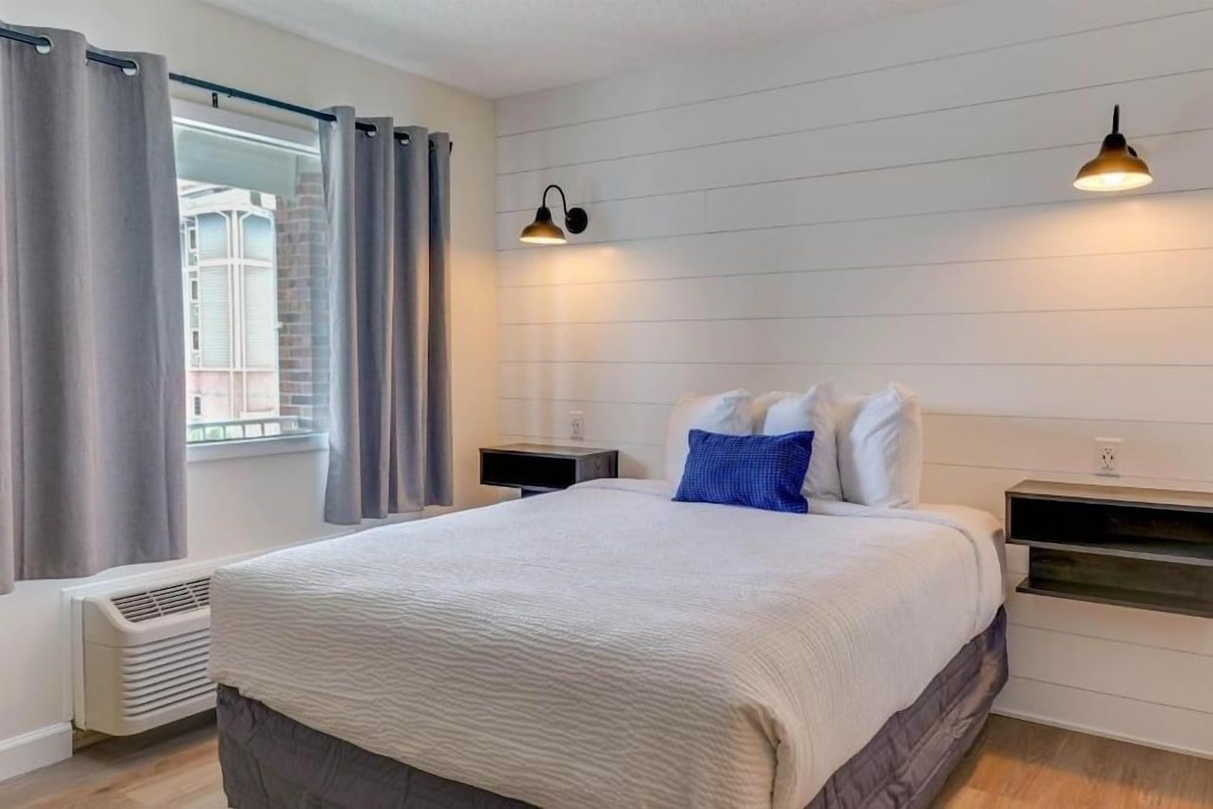 A hotel room with a bed, bedside tables, a heater, curtains, and a window with a view.