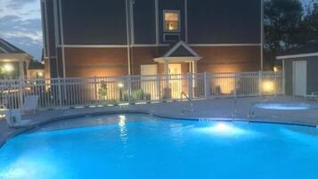 A swimming pool with a white fence, a building with a balcony, and a small structure with a door.