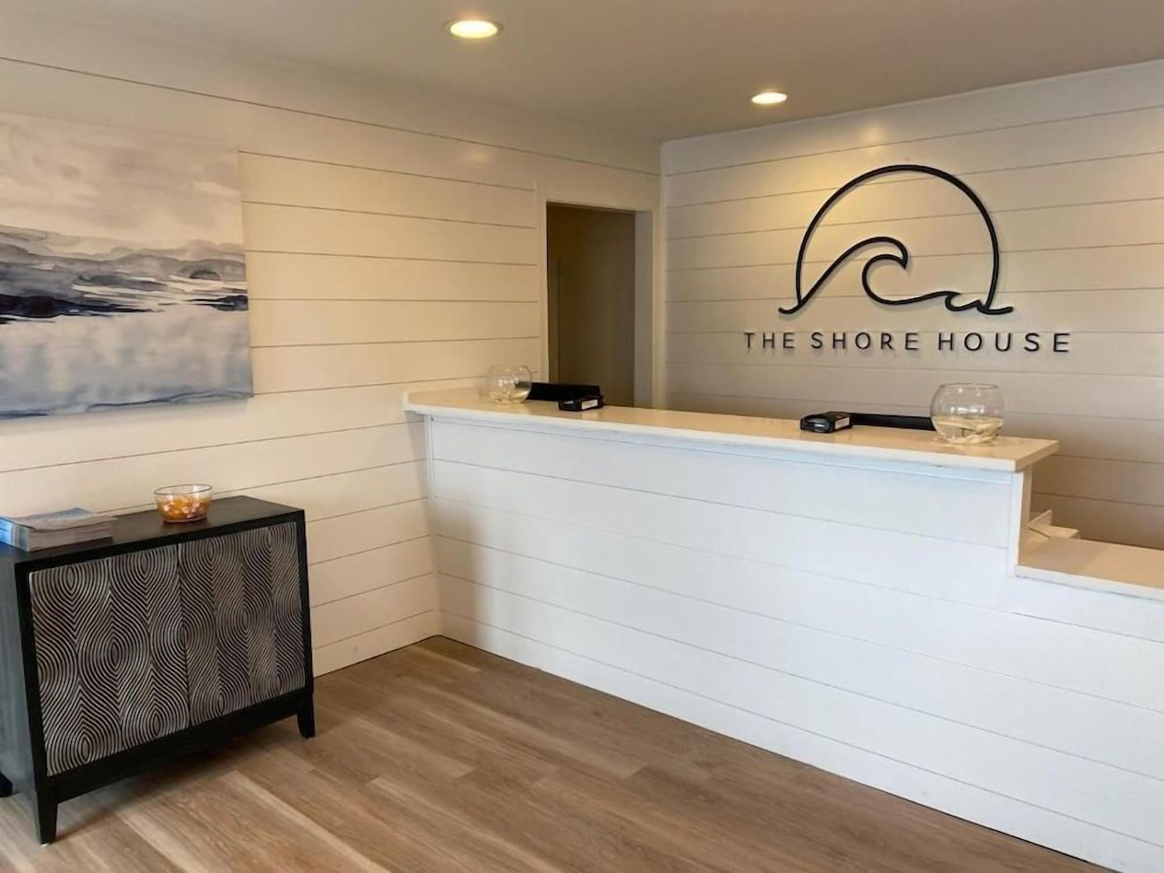 A reception desk with a logo above it, a painting on the wall, and a patterned side table.