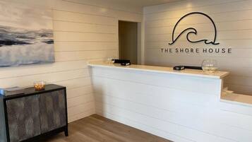 A reception desk with a logo above it, a painting on the wall, and a patterned side table.