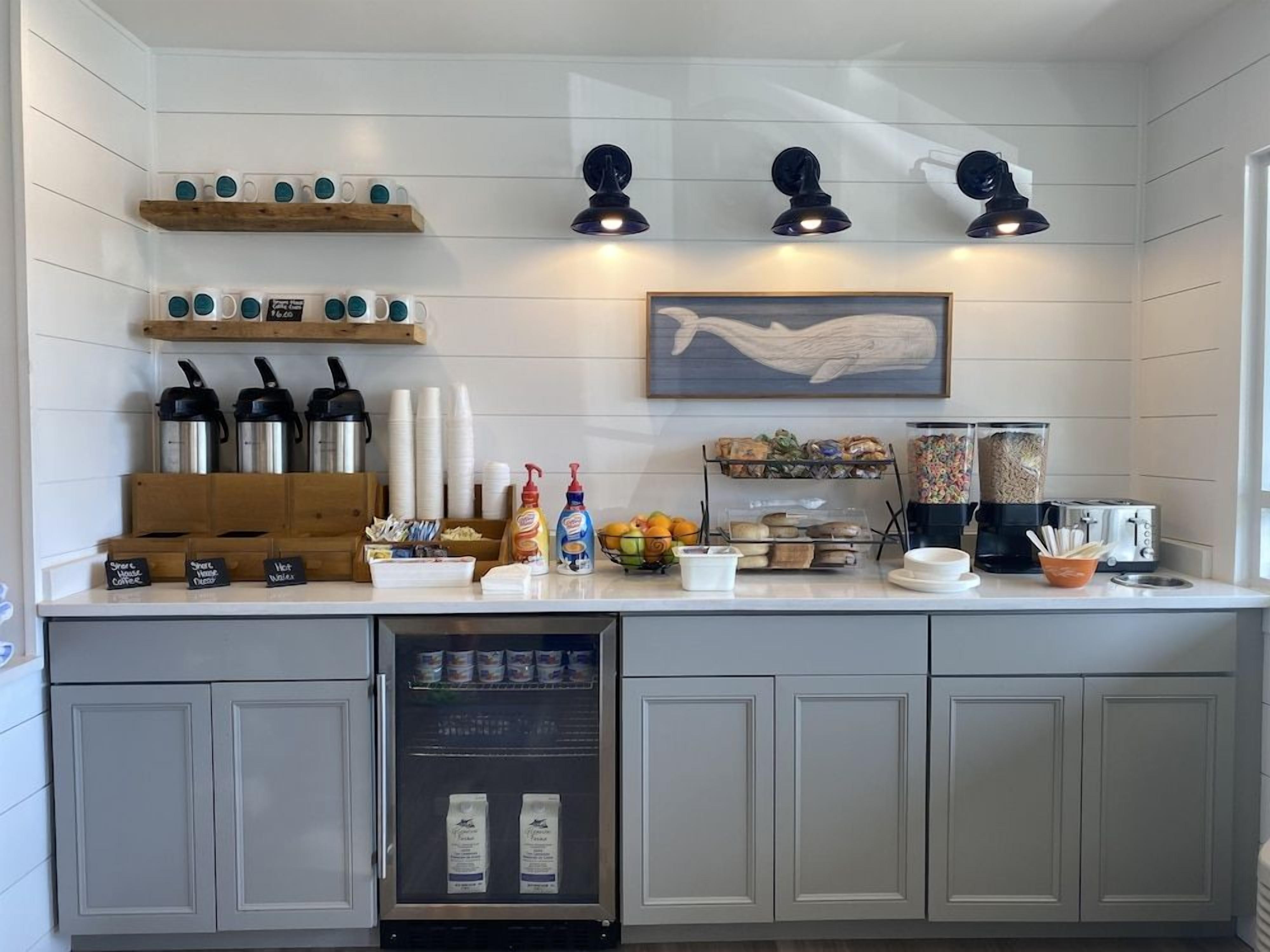 A kitchen with a white countertop, coffee machines, a refrigerator, and a microwave.