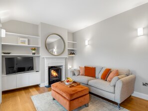 Ein modernes Wohnzimmer mit Kamin, einer Couch, einem Hocker und einem Flachbildfernseher.