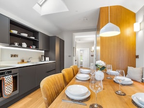 A modern kitchen with dark cabinetry, a wooden dining table set for six, and a pendant light. - Market Street Apartment, Clifden (Clifden)