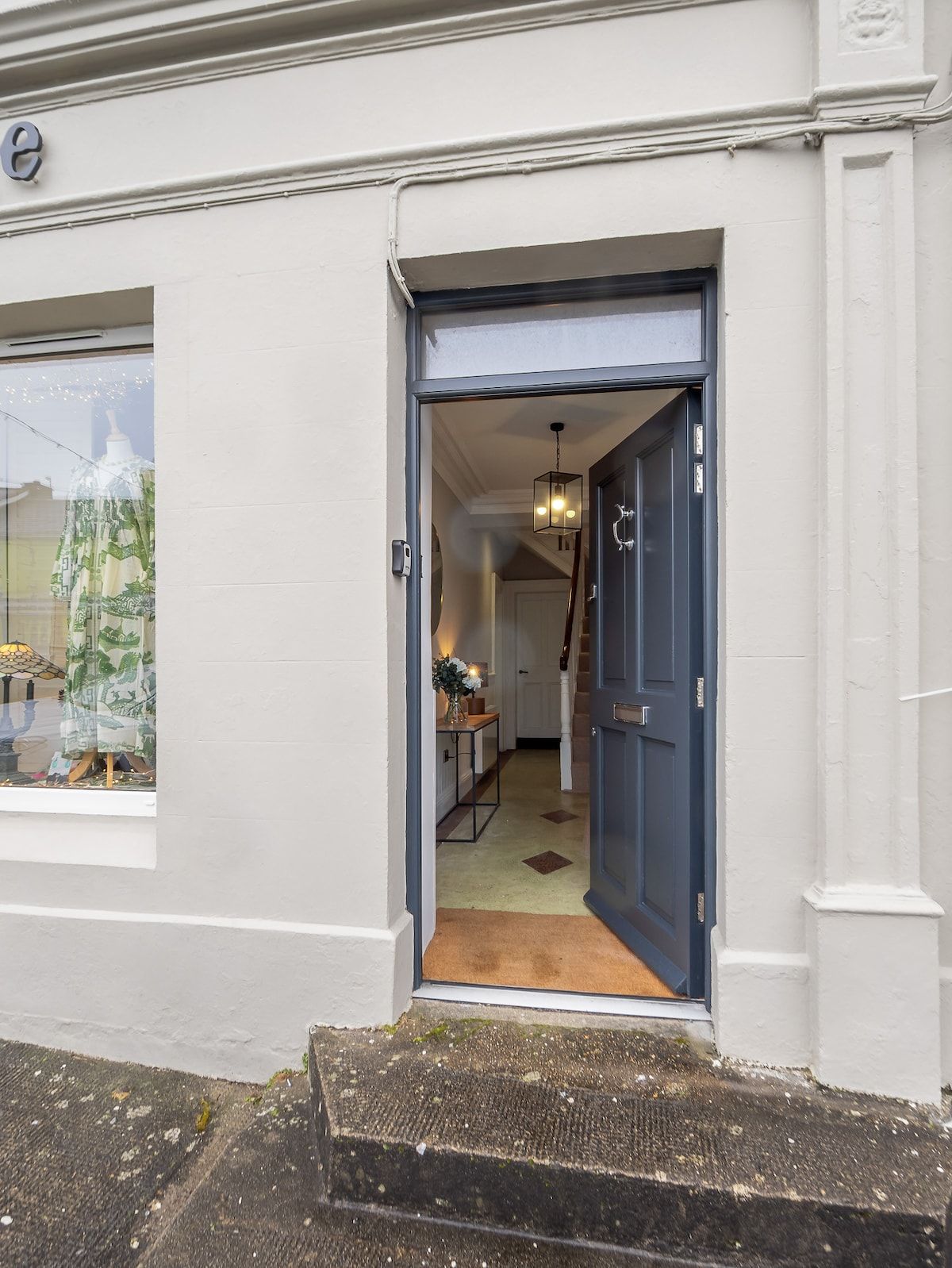 A doorway leading into a room with a table and a chair, a hanging light fixture, and a door with a handle.