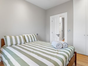 A bedroom with a bed, pillows, a rolled towel, and a wardrobe. - Market Street Apartment, Clifden (Clifden)