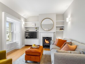 A living room with a fireplace, a television, and a sofa with cushions. - Market Street Apartment, Clifden (Clifden)