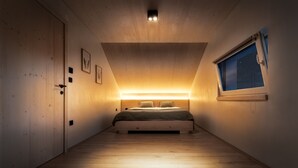 A bedroom with a wooden floor, a bed with a headboard, a window with a view of the night sky, and a door on the left. - Herb Haven Cottage With a View (Pesnica)