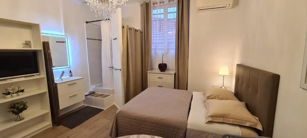 A modern hotel room with a bed, bedside table, TV, and a shower area.