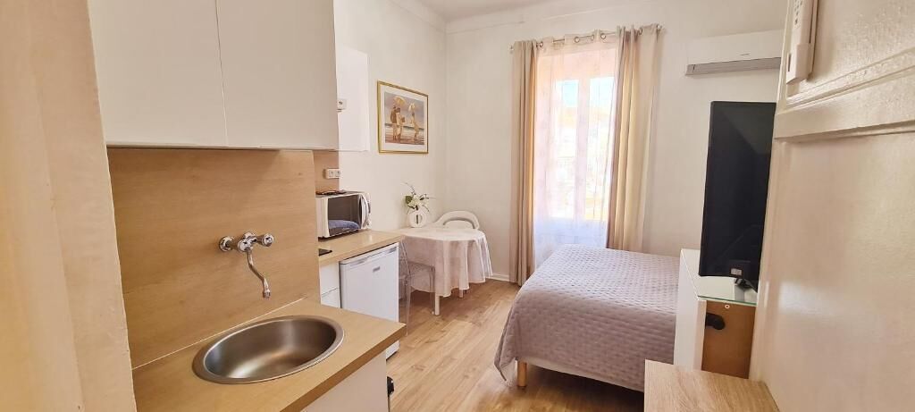 Kompakti hotellihuone, jossa on pieni keittiönurkkaus, sänky, televisio ja pieni pöytä tuolilla.