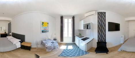 A modern hotel room with a bed, a small table, a chair, a kitchenette, and a TV.