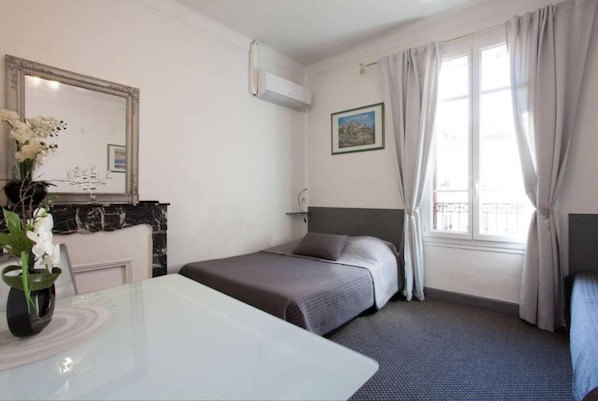 Une chambre d’hôtel avec un lit, une table de chevet, un miroir, une fenêtre avec des rideaux et un tableau au mur.