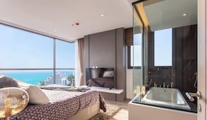 A modern bedroom with a large bed, a TV, and a glass-enclosed bathroom with a bathtub. - Luxury 2 Bed Room Sea View - Excellent Location (Pattaya)