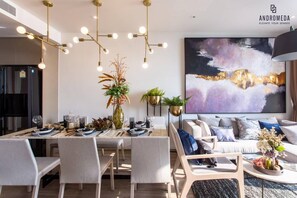 A modern dining area with a long table set for six, surrounded by chairs. There is a large painting on the wall above the table, and a sofa with cushions in the background. - Luxury 2 Bed Room Sea View - Excellent Location (Pattaya)