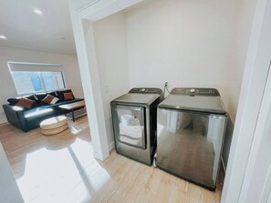 A modern kitchen with stainless steel appliances, a wooden floor, and a dark-colored sofa with cushions. - Cozy 3/2 Rose Bowl, Pasadena with AC and Parking (Altadena)