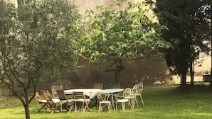 Un espace extérieur aménagé pour les repas, avec une table et des chaises, entouré de pelouse et d’arbres.