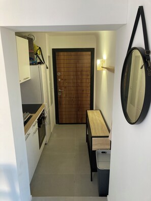 A compact kitchen with a wooden door, a small table, and a hanging mirror. - Cosy T2 apartment with superb pergola terrace and maquis view (Pianottoli-Caldarello)