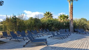Een houten terras met rijen zwarte loungestoelen.