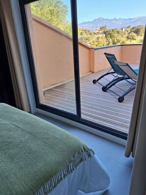 Quarto com grande janela com vista para um deck com piscina e cadeiras.