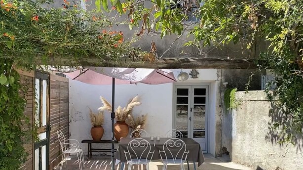 Une terrasse avec une table et des chaises, des plantes en pot et une porte.