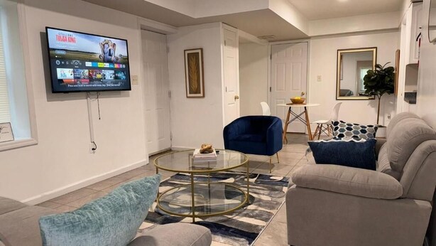 Ein modernes Wohnzimmer mit einem wandmontierten Flachbildfernseher, einem Glastisch und zwei Sofas mit Kissen.