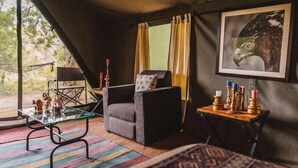 A cozy room with a cushioned chair, a glass table, and a small side table with candles. - Mahoora Tented Safari Camp Udawalawe (Udawalawa)