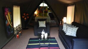 A cozy room with a black sofa, a small table with a candle, and a colorful painting on the wall. - Mahoora Tented Safari Camp Udawalawe (Udawalawa)