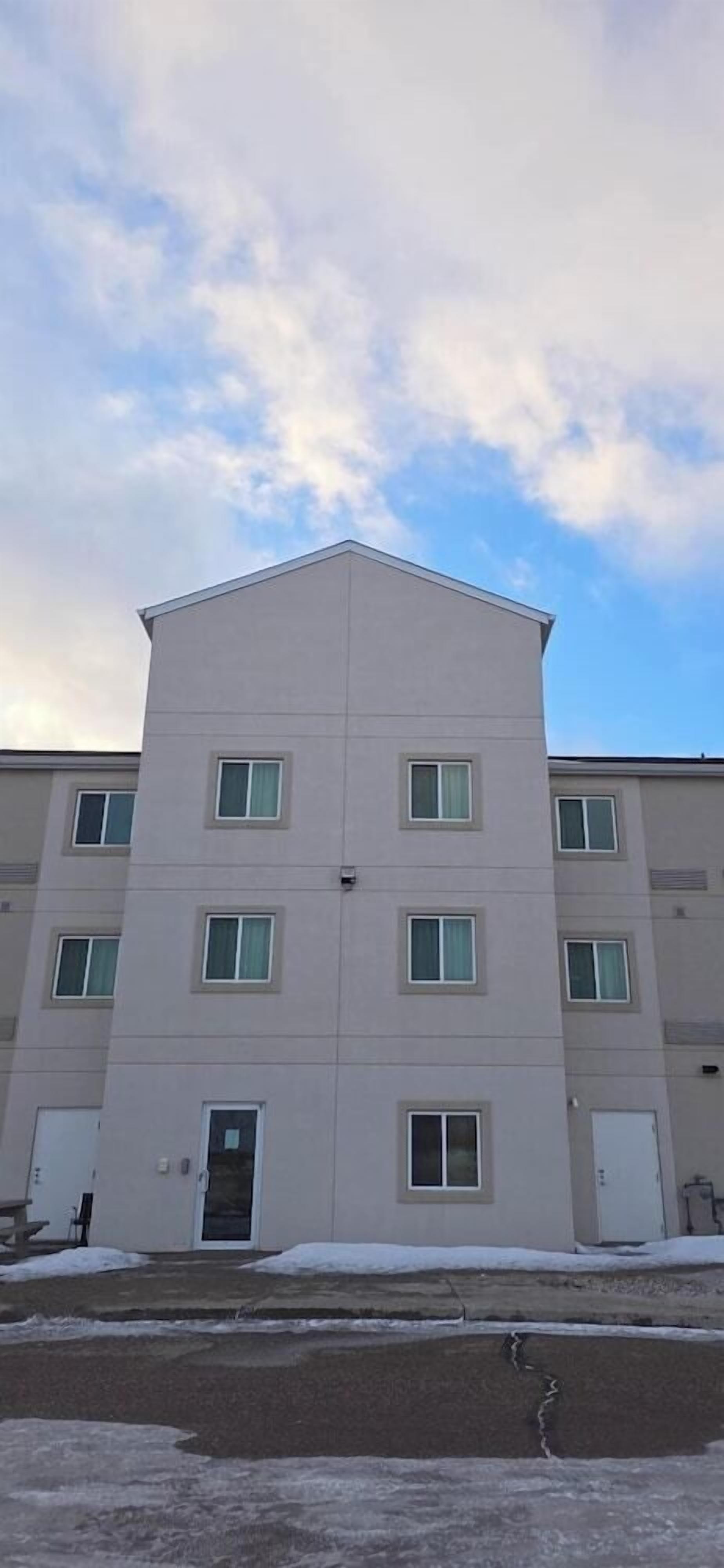 A multi-story building with a flat roof, rectangular windows, and a door at the ground level.