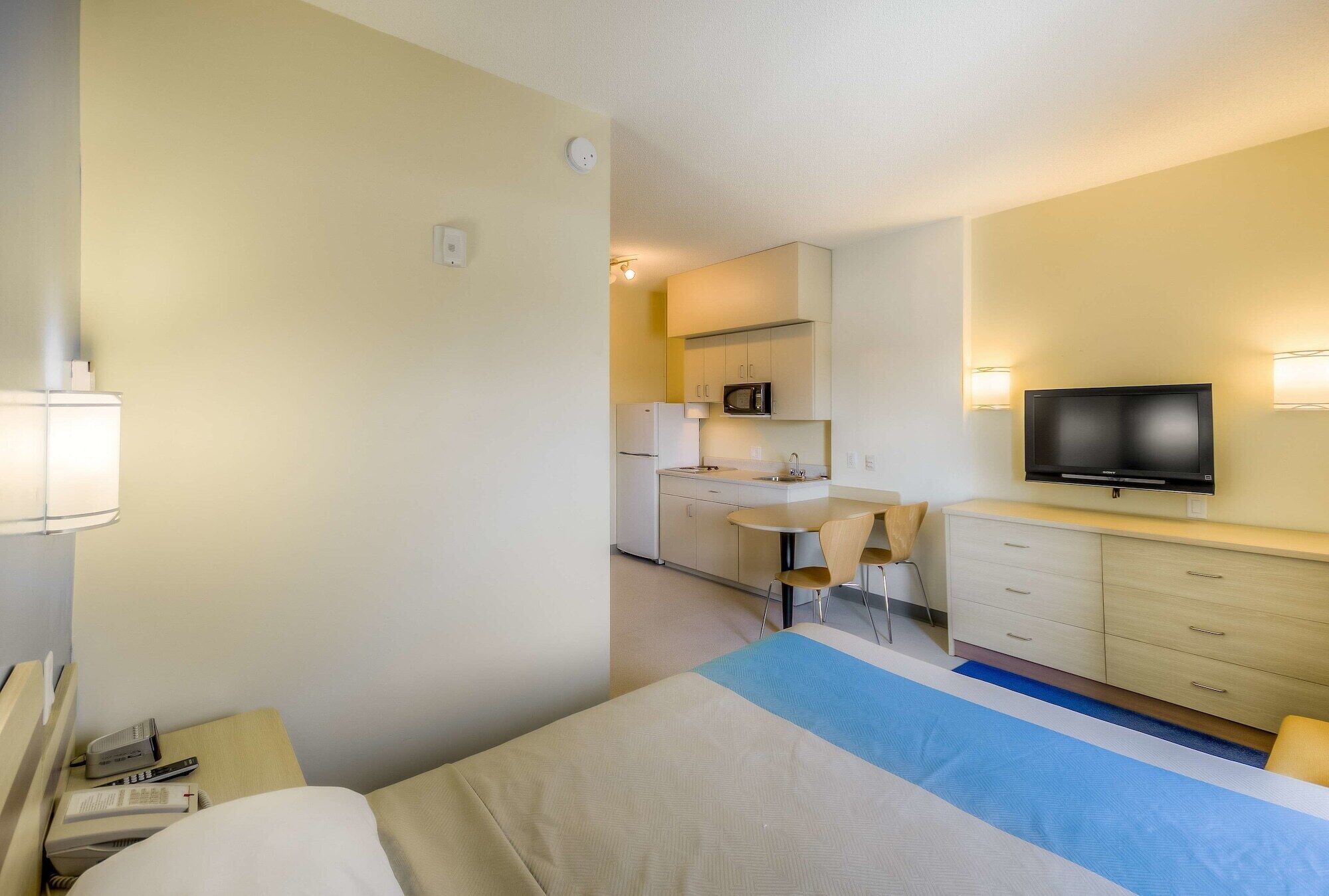 Une chambre d’hôtel équipée d’un lit, d’un bureau, d’un four à micro-ondes, d’un réfrigérateur, d’une télévision et d’une petite kitchenette.
