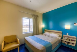 A hotel room with a bed, a chair, a bedside table with a phone, and a window with curtains. - Super 8 by Wyndham Estevan (Estevan)