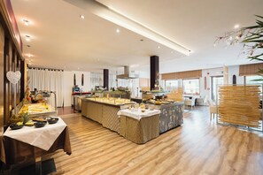 A spacious hotel dining area with a buffet setup, wooden flooring, and a modern kitchen in the background. - Residence GoldRain (Laces)