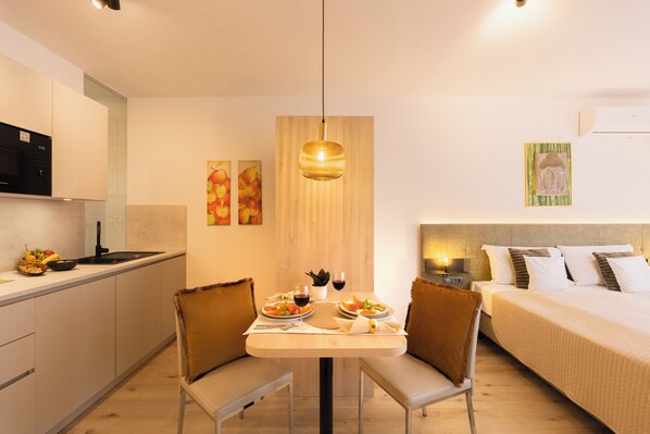 A modern hotel room with a kitchenette, a dining table with chairs, a bed, and a hanging light fixture. - Residence GoldRain (Laces)