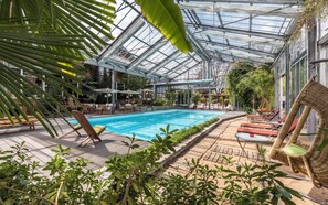 An indoor swimming pool with a glass ceiling, surrounded by lounge chairs and potted plants. - Residence GoldRain (Laces)